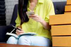 特写镜头年轻的亚洲女人企业家电话写作订单客户在线笔记本在线购物物流交付女卖方工作沙发业务锻造