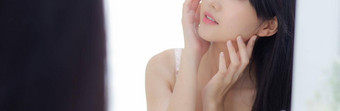 美丽的年轻的亚洲女人镜子检查脸皮肤护理化妆品卫生美女孩快乐清洁面部奶油乳液健康横幅网站
