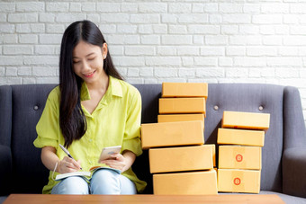 年轻的亚洲女人企业家电话写作订单客户在线笔记本首页在线购物物流交付女卖方工作沙发业务锻造