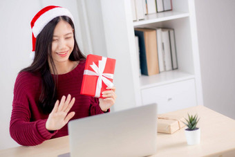 年轻的亚洲女人自拍<strong>视频</strong>调用在线朋友显示红色的礼物盒子圣诞节一天相机首页社会距离正常的女<strong>视频</strong>会议沟通<strong>假期</strong>