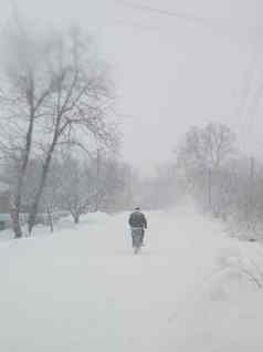 雪暴雪村男人。骑自行车街