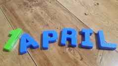 塑料彩色的字母使单词4月木地板上