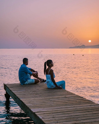 克里特岛希腊年轻的浪漫的夫妇爱坐着拥抱木码头海滩日出时间金天空假期旅行概念浪漫的年轻的夫妇约会海边