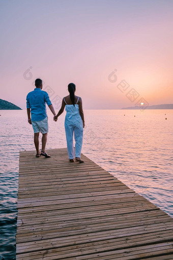克里特岛希腊年轻的浪漫的夫妇爱坐着拥抱木码头海滩日出时间金天空假期旅行概念浪漫的年轻的夫妇约会海边
