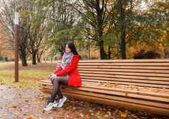 年轻的女孩红色的外套坐着板凳上城市公园