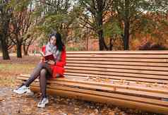 年轻的女孩阅读书坐着公园板凳上