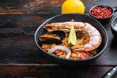 自制的新鲜准备西班牙海鲜饭王虾贻贝鱿鱼黑色的碗黑暗木背景复制空间