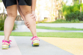 女高脂肪的跑步者运动员腿受伤疼痛手抓住痛苦的腿运行公园