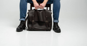男人。蓝色的牛仔裤黑色的靴子坐在椅子棕色（的）男人的肩膀皮革袋文档移动PC白色地板上犯罪皮革书包信使袋手工制作的公文包
