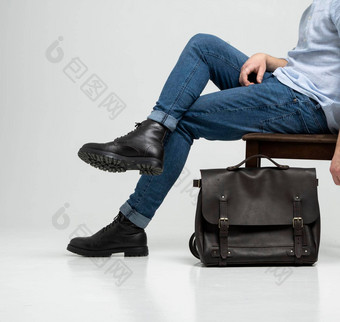 男人。蓝色的牛仔裤黑色的靴子坐在椅子棕色（的）男人的肩膀皮革袋文档移动PC白色地板上犯罪皮革书包信使袋手工制作的公文包