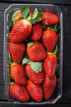红色的成熟的草莓清晰的塑料托盘黑色的木表格背景前视图平躺