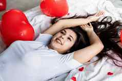 年轻的快乐浅黑肤色的女人女人铺设床上红色的心形状的气球装饰