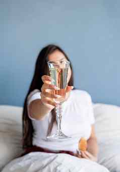 年轻的浅黑肤色的女人女人坐着醒着的床上红色的心形状的气球装饰喝香槟吃羊角面包