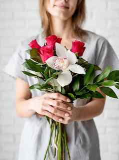 年轻的女人持有兰花玫瑰花束