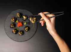 手筷子持有寿司自定义寿司卷黑色的大米蟹肉鳄梨烟熏大马哈鱼摩丝桨鱼子酱大规模虾鸡尾酒可食用的黄金叶姜芥末酱黑色的表格