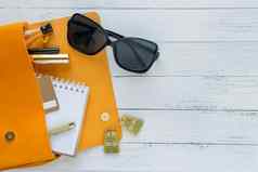 时尚概念女的事情化妆品产品太阳镜笔记本橙色手提包木背景Copyspace平躺前视图