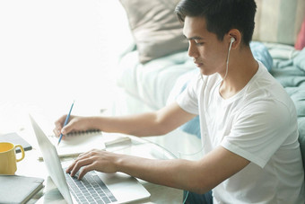 亚洲年轻的学生男人。企业家穿耳机工作电脑研究学习在线首页电子学习网络研讨会会议社会距离科维德流感大流行