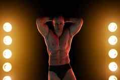 活跃的生活方式概念专业健美运动员显示完美的肌肉发达的身体灯照明背景