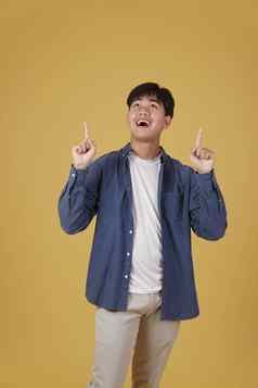 肖像快乐年轻的亚洲男人。穿着随便指出手指Copyspace黄色的背景