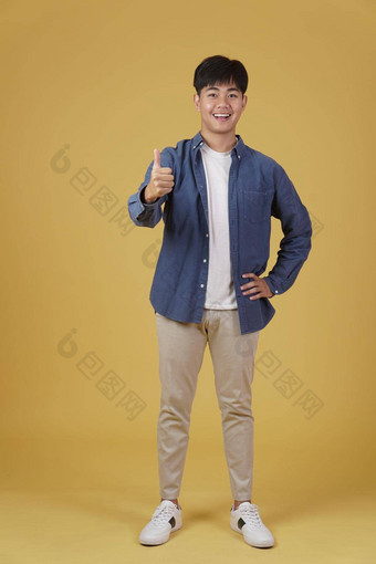 肖像微笑积极的年轻的亚洲男人。穿着随便拇指手势批准表达式孤立的黄色的背景