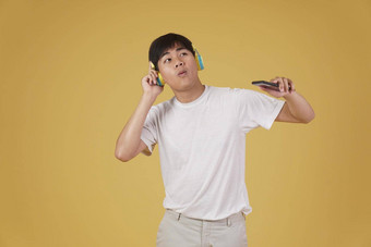 肖像快乐快乐的快乐的年轻的亚洲男人。穿耳机听音乐智能手机跳舞孤立的黄色的背景