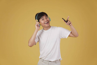 肖像快乐快乐的快乐的年轻的亚洲男人。穿耳机听音乐智能手机跳舞孤立的黄色的背景