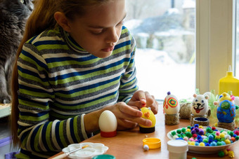 女孩坐在表格窗口油漆复活节鸡蛋刷油漆
