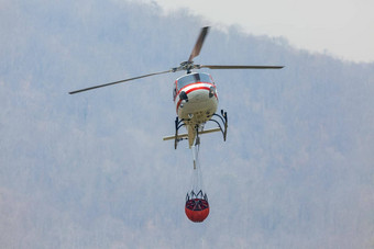 消防直升机携带水桶扑灭森林火复出湖填充水