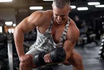 肌肉发达的运动健美运动员健身模型坐着板凳上培训肱二头肌电梯哑铃室内健身房