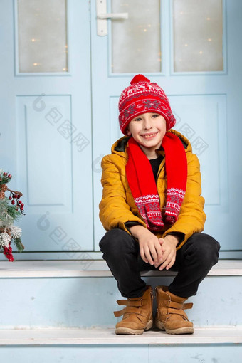 英俊的男孩明亮的冬天衣服坐在玄关房子