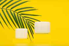 奶油罐子黄色的基座黄色的背景棕榈叶概念夏天护肤品防晒系数