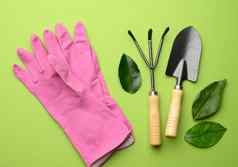粉红色的橡胶手套花园集铲子耙子干草叉绿色背景