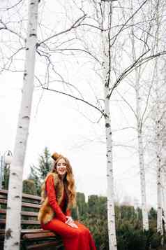 年轻的女孩红色的头发明亮的红色的衣服板凳上空公园