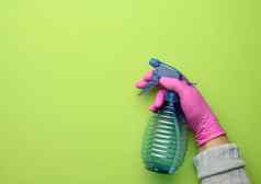 女手粉红色的手套持有透明的塑料喷雾瓶绿色背景