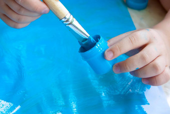 孩子的手持有下降刷油漆涂片蓝色的油漆白色纸