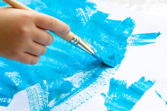 孩子的手持有刷油漆纸大中风涂片蓝色的油漆白色纸