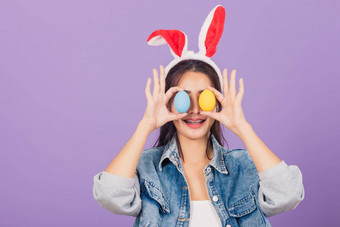 女人微笑穿兔子耳朵工装裤持有色彩斑斓的复活节鸡蛋前面眼睛