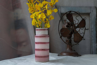 花束黄色的花粉红色的手工制作的陶瓷花瓶古董风扇白色变形表格布水泥墙