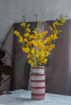 花束黄色的花粉红色的手工制作的陶瓷花瓶古董风扇白色变形表格布水泥墙