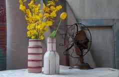 花束黄色的花手工制作的陶瓷花瓶古董风扇白色变形表格布水泥墙