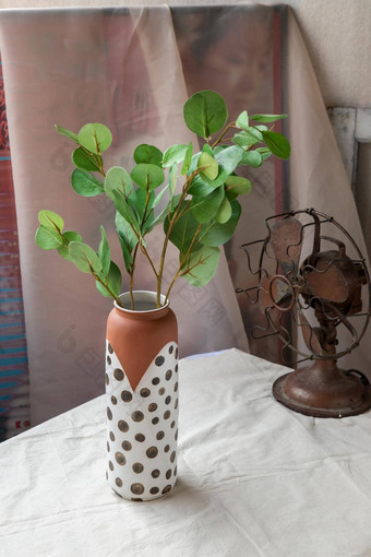 绿色叶手工制作的陶瓷花瓶古董风扇白色变形表格布水泥墙