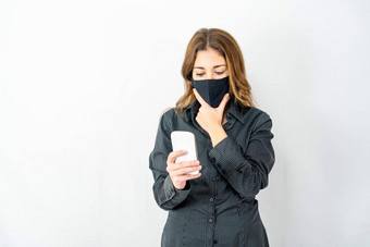 年轻的模型女人孤立的白色背景穿业务黑暗衬衫保护面具下巴担心智能手机阅读最新的冠状病毒新闻科维德女孩表达式