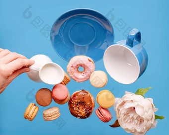 空蓝色的杯甜甜圈蛋白杏仁饼牡丹手持有牛奶奶油壶飞行蓝色的背景