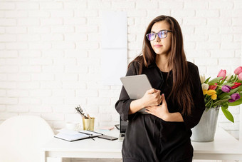 肖像年轻的自信浅黑肤色的女人业务女人站桌子上新鲜的郁金香持有数字平板电脑