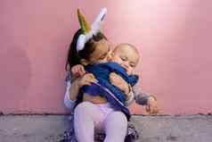 可爱的女孩穿独角兽头巾拥抱接吻婴儿