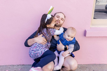 快乐父亲持有可爱的女儿粉红色的墙背景