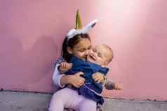 可爱的女孩穿独角兽头巾拥抱接吻婴儿