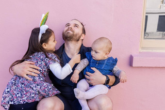快乐父亲拥抱可爱的女儿前面粉红色的墙