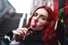 迷人的十几岁的女孩红色的头发舔甜蜜的草莓糖果墙涂鸦