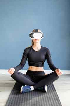 年轻的金发女郎女人体育运动衣服穿虚拟现实眼镜冥想健身席